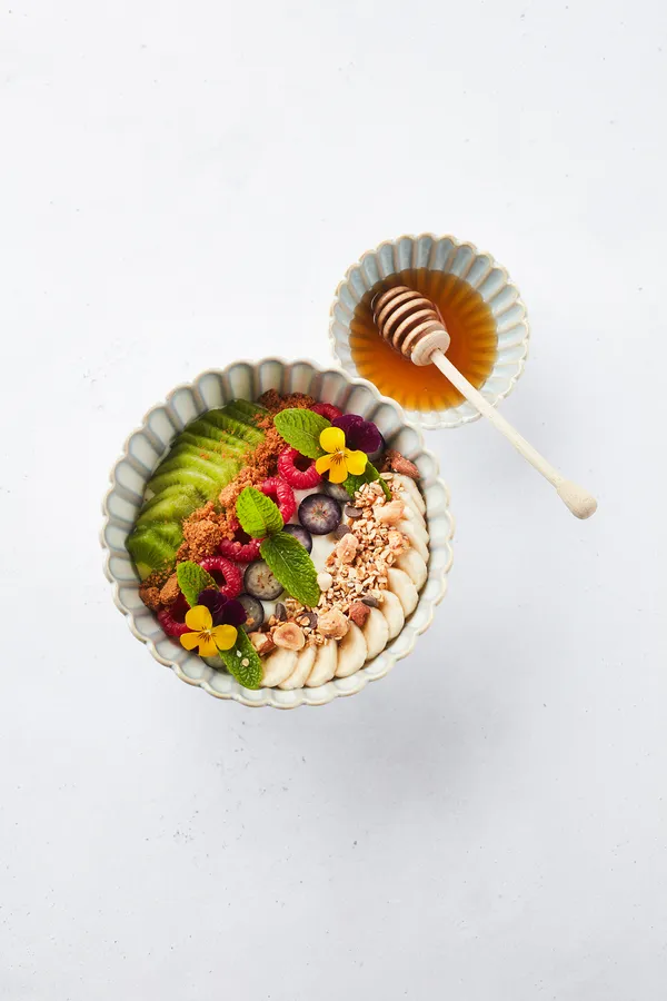 Bowl met fruit, noten en bloemetjes, naast een kommetje honing